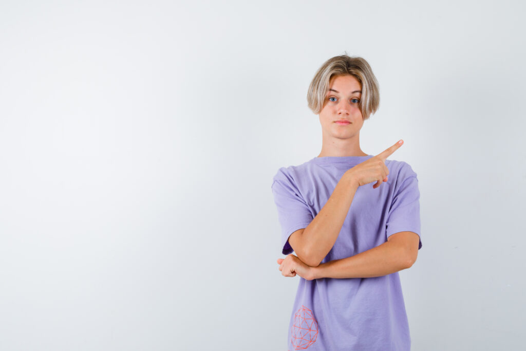 Teen boy pointing at upper right corner in t shirt and looking confident. front view.
